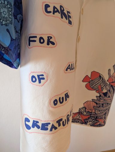 Bluse mit Meeresmotiv und Kraken auf dem Rücken, Fokus auf das Vorderteil mit Textzug "Care for all of our creatures"